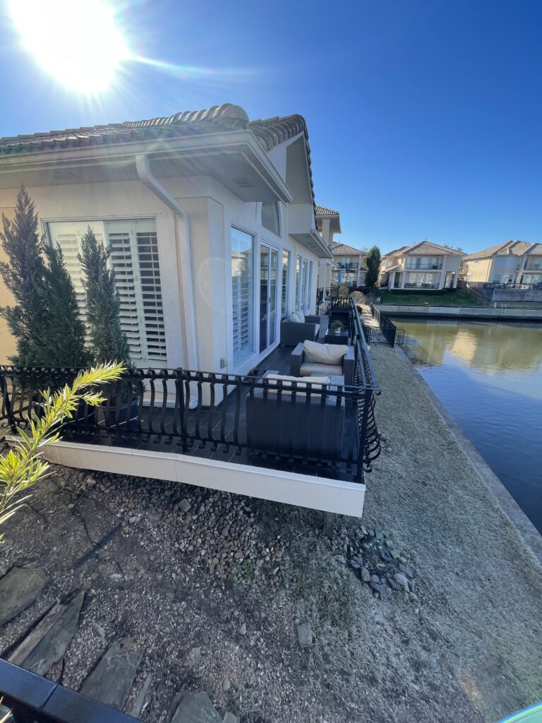 A white house with a black fence overlooking a calm waterfront.